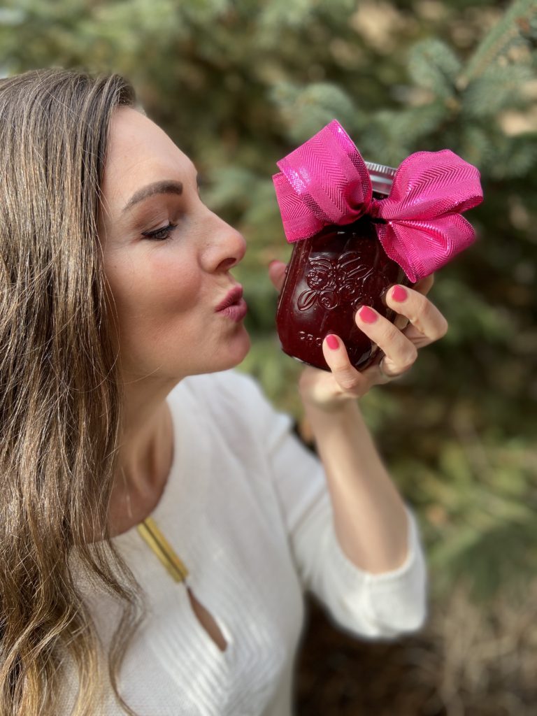 Brunette woman almost kissing a jar of Homemade Strawberry Jam with a pink ribbon tied around the top.