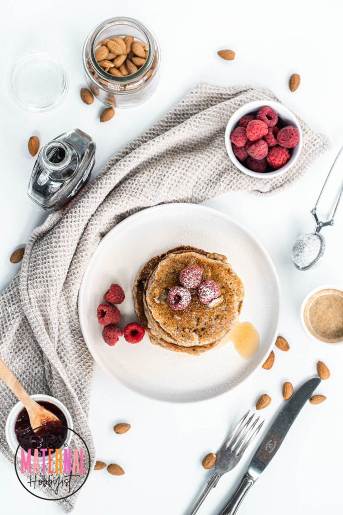 gluten free pancakes made with almonds sitting on a plate, topped with raspberries and syrup.