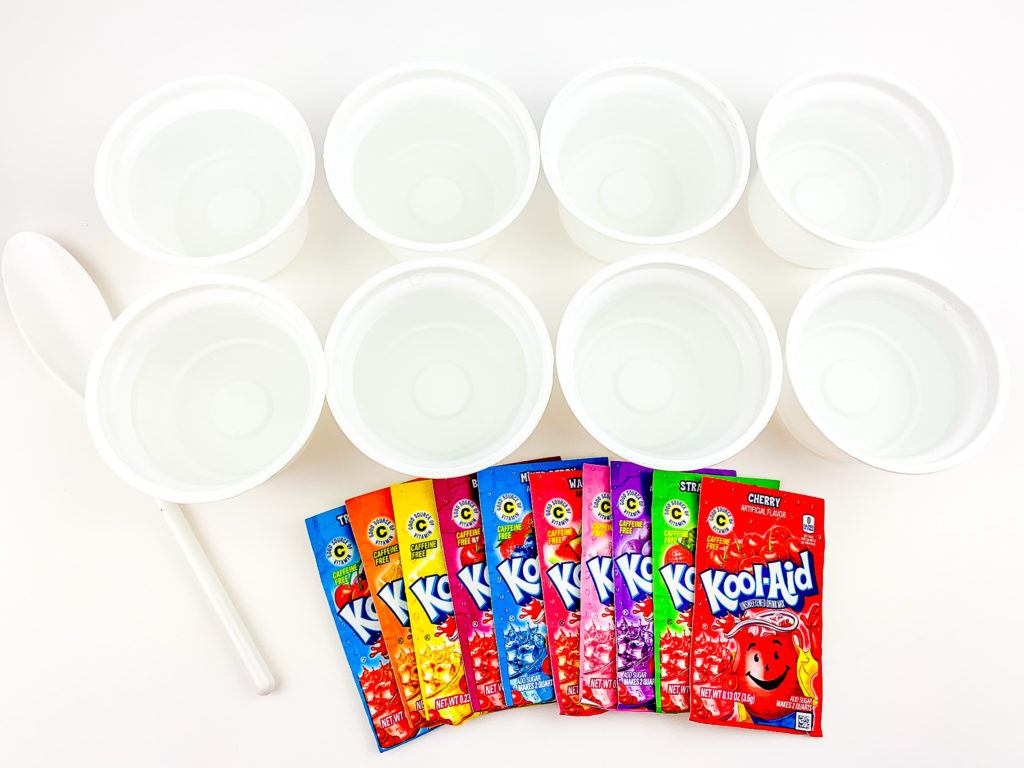 8 recycled yogurt cups filled with clean water next to Kool-aid packets and a spoon