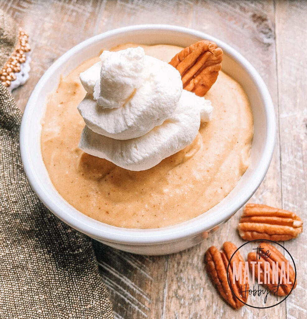 Creamy Pumpkin Mousse with Maple Whipped Cream inside a white bowl topped with a pecan