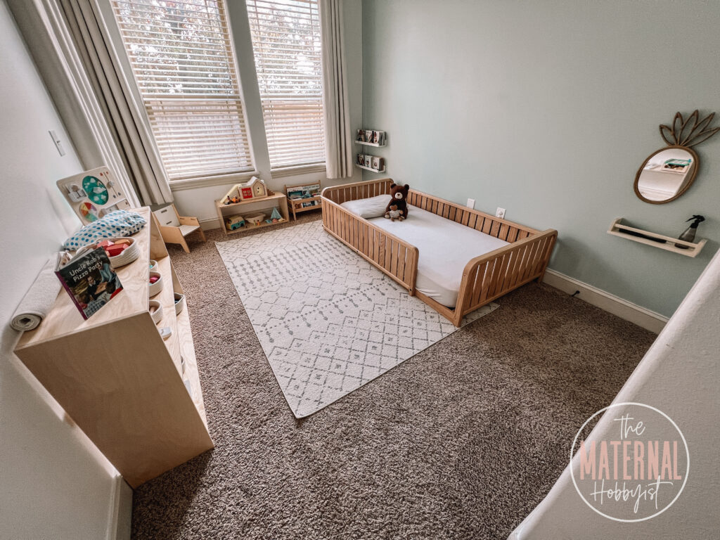 full view photo of a Montessori toddler bedroom with a floor bed, birch shelves filled with toys, and book shelves filled with books.