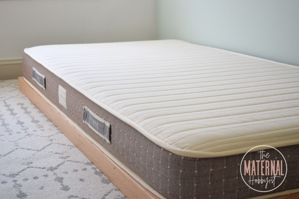 6" organic cotton mattress sitting on top of a brown montessori toddler floor bed platform frame in a bedroom.