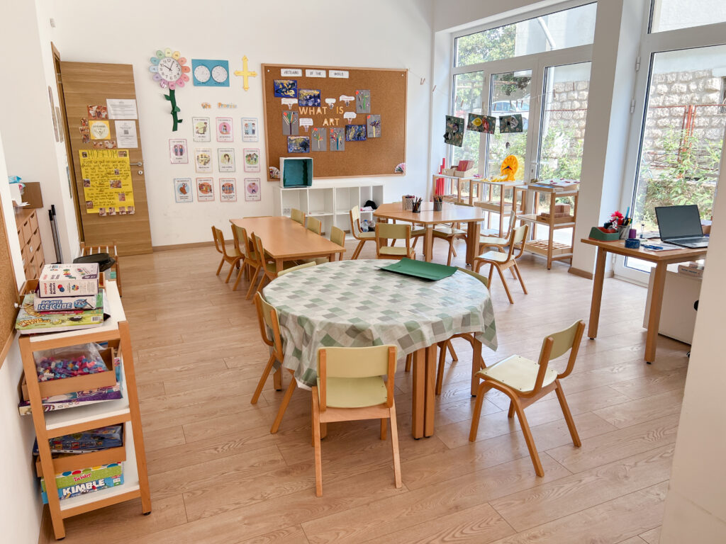 Explorers ages 4 to 5 classroom tables with chairs, with shelves filled with Montessori manipulatives for learning